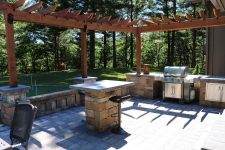 Backyard kitchen with stone floor and wood pergola