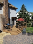 Tan backyard deck with three steps down to brick patio